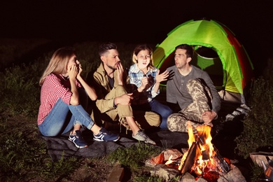 Woman with flashlight telling scary story for her friends near bonfire at night. Camping season
