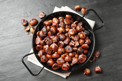 Delicious roasted edible chestnuts on black slate table, flat lay