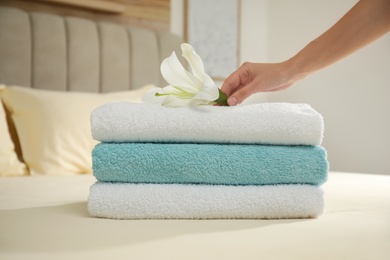 Woman putting flower on stack of clean towels in bedroom, closeup