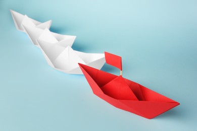 Photo of Group of paper boats following red one on light blue background. Leadership concept