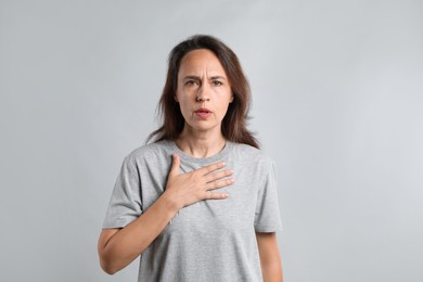 Mature woman suffering from breathing problem on light background