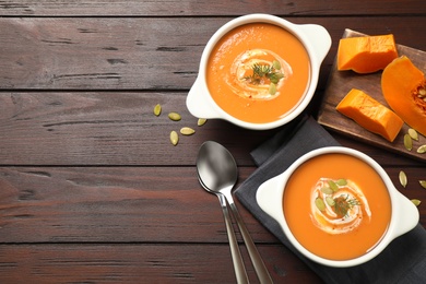 Tasty creamy pumpkin soup with dill and seeds in bowls on wooden table, flat lay. Space for text
