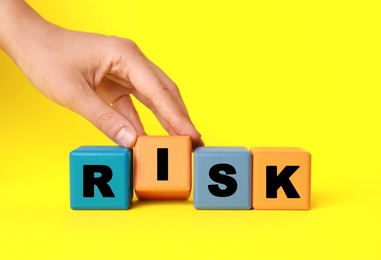 Woman making word Risk with colorful cubes on yellow background, closeup