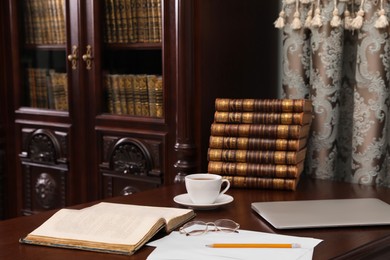 Photo of Laptop, books and cup of coffee on wooden table in library reading room