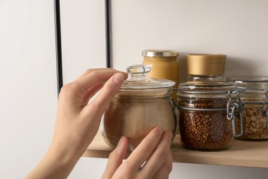 Woman taking glass jar of buckwheat flour from shelf, closeup