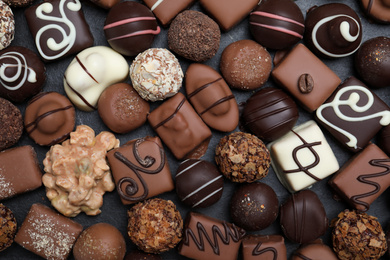 Different delicious chocolate candies on black table, flat lay