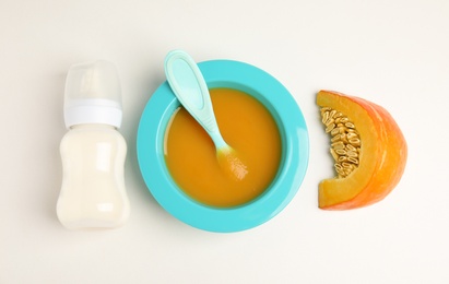 Baby food in bowl and fresh ingredients on white table, flat lay