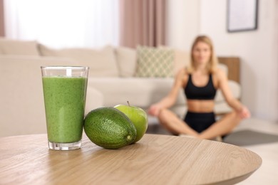 Photo of Young woman in fitness clothes doing exercise at home, focus on glass of smoothie and fruits