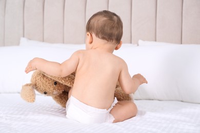 Cute baby in dry soft diaper with toy bunny on white bed at home, back view