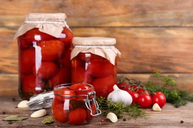 Glass jars of pickled tomatoes and ingredients on wooden table. Space for text