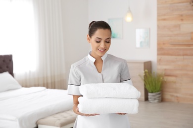 Young chambermaid with clean towels in bedroom