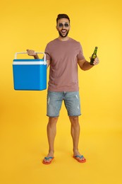 Happy man with cool box and bottle of beer on yellow background