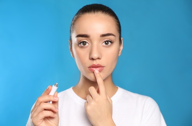 Photo of Woman with herpes applying cream on lips against light blue background