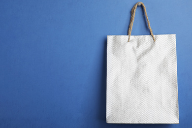 Silver shopping paper bag on blue background, space for text