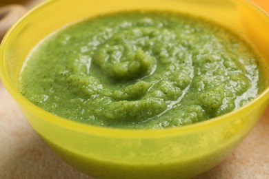 Photo of Baby food. Bowl with tasty broccoli puree on beige textured table, closeup