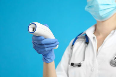 Doctor holding non contact infrared thermometer against light blue background, focus on hand. Measuring temperature