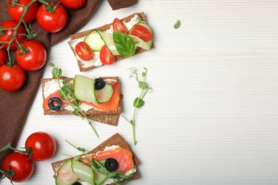 Tasty rye crispbreads with salmon, cream cheese and vegetables on white wooden table, flat lay. Space for text