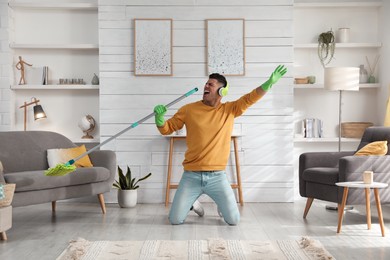 Man in headphones with mop singing while cleaning at home