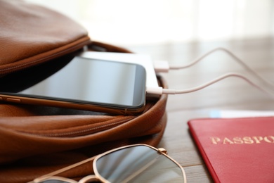 Charging mobile phone with power bank in backpack on wooden table, closeup
