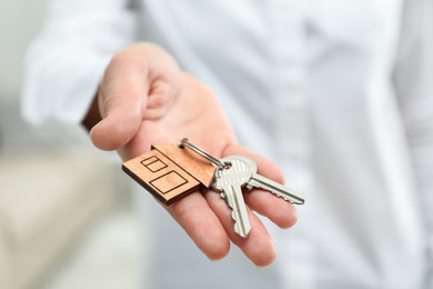 Real estate agent holding house keys with trinket, closeup