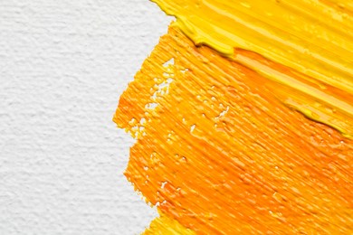 Photo of Beautiful strokes of yellow and orange oil paints on white canvas, closeup