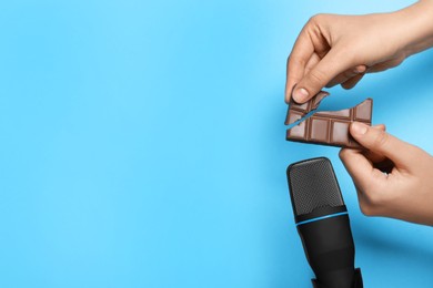 Woman making ASMR sounds with microphone and chocolate on light blue background, closeup. Space for text