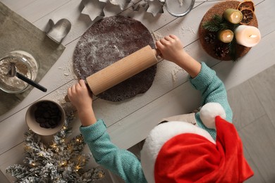 Little child rolling dough for Christmas cookies at white wooden table, top view