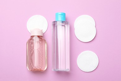Flat lay composition with bottles of micellar water and cotton pads on pink background