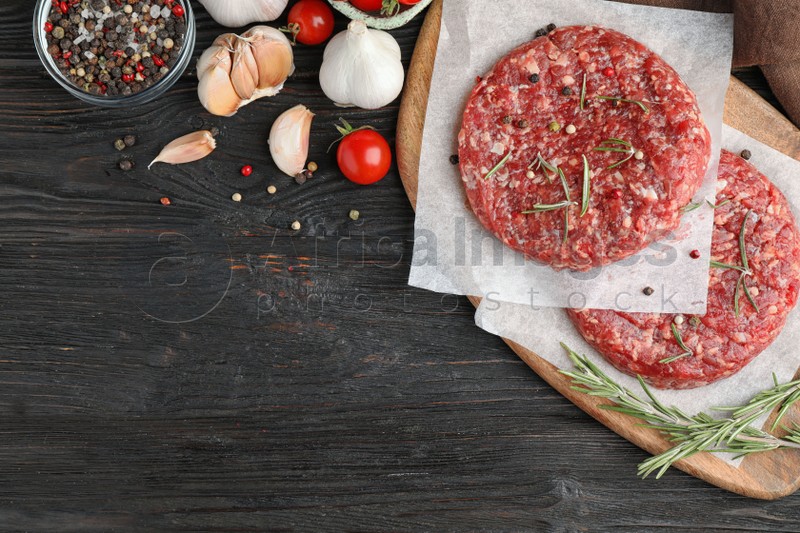 Flat lay composition with raw meat cutlets for burger on black wooden table. Space for text