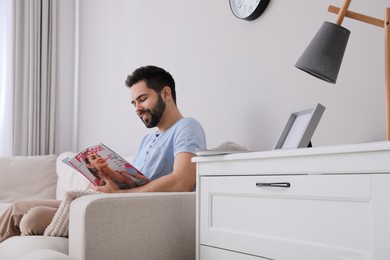 Young man reading sports magazine on sofa at home