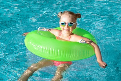 Happy little girl with inflatable ring in outdoor swimming pool on sunny day