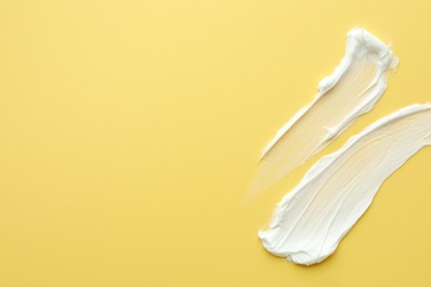 Samples of face cream on yellow background, top view. Space for text