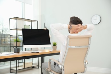 Young businessman relaxing in office chair at workplace, back view. Space for text