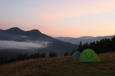 Picturesque view of mountain landscape with fog and camping tents in early morning