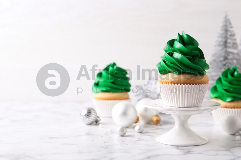 Photo of Delicious cupcakes with green cream and Christmas decor on white marble table. Space for text
