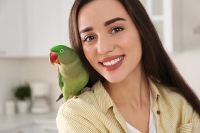 Young woman with Alexandrine parakeet indoors. Cute pet