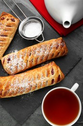 Photo of Fresh tasty puff pastry with sugar powder and tea served on grey table, flat lay