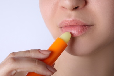 Woman applying hygienic lipstick on lips against white background, closeup