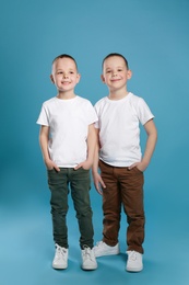 Full length portrait of cute twin brothers on color background