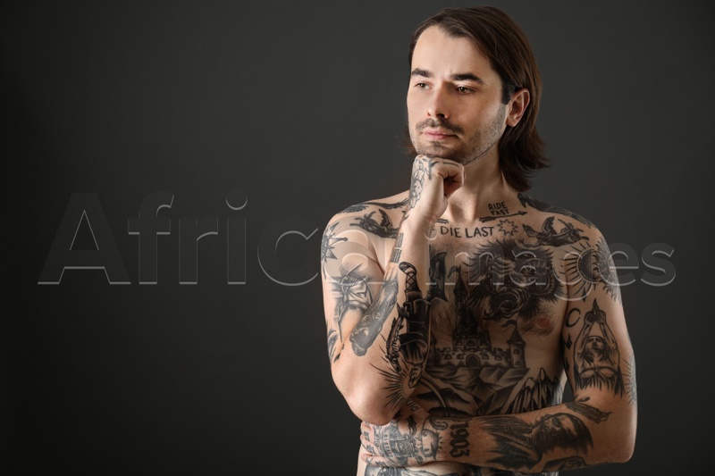 Young man with tattoos on body against black background. Space for text