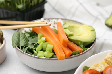 Photo of Delicious poke bowl with basil, vegetables and avocado on light grey table, closeup