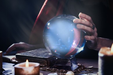 Photo of Soothsayer using crystal ball to predict future at table in darkness, closeup. Fortune telling