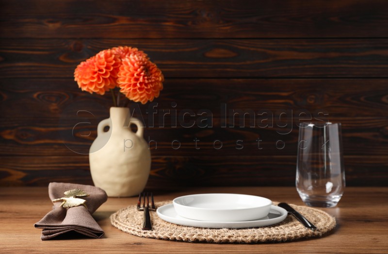 Beautiful cutlery, plate, glass, napkin with ring and flowers in vase on wooden table
