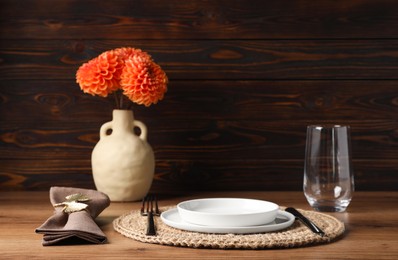 Photo of Beautiful cutlery, plate, glass, napkin with ring and flowers in vase on wooden table
