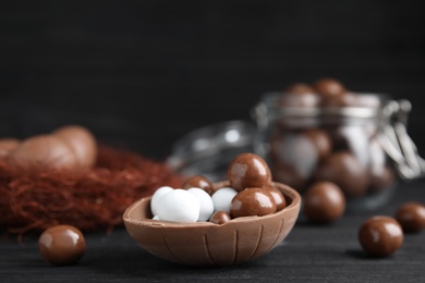 Half of tasty chocolate egg with candies on black wooden table, space for text
