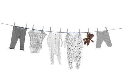 Different baby clothes and toy drying on laundry line against white background
