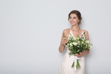 Young bride wearing wedding dress with beautiful bouquet on light grey background. Space for text