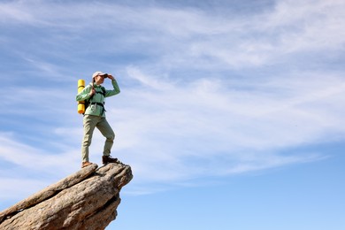 Young woman with backpack on rocky peak in mountains. Space for text