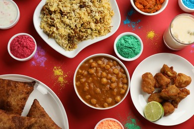 Traditional Indian food and color powder dyes on red background, flat lay. Holi festival
