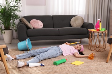 Tired young woman sleeping and cleaning supplies on floor in living room